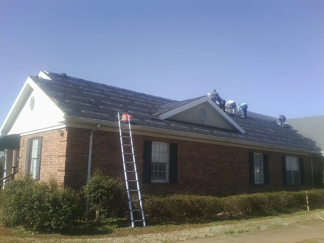 Crew tearing shingles off a brick ranch roof with a ladder set — Metal Roof Repair work by our crew in Culver