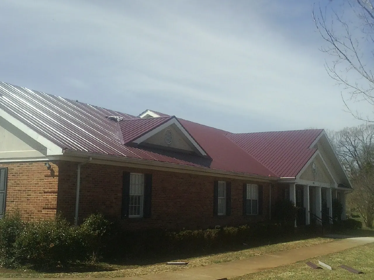 Red metal roof with gabled entries on a long brick building, from a Hail Damage Roof Repair job in Culver