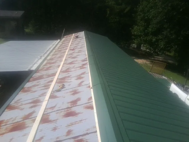 Old rusted panels beside newly installed green metal roofing — Wind Damage Roof Repair by Roofing Brothers in Culver
