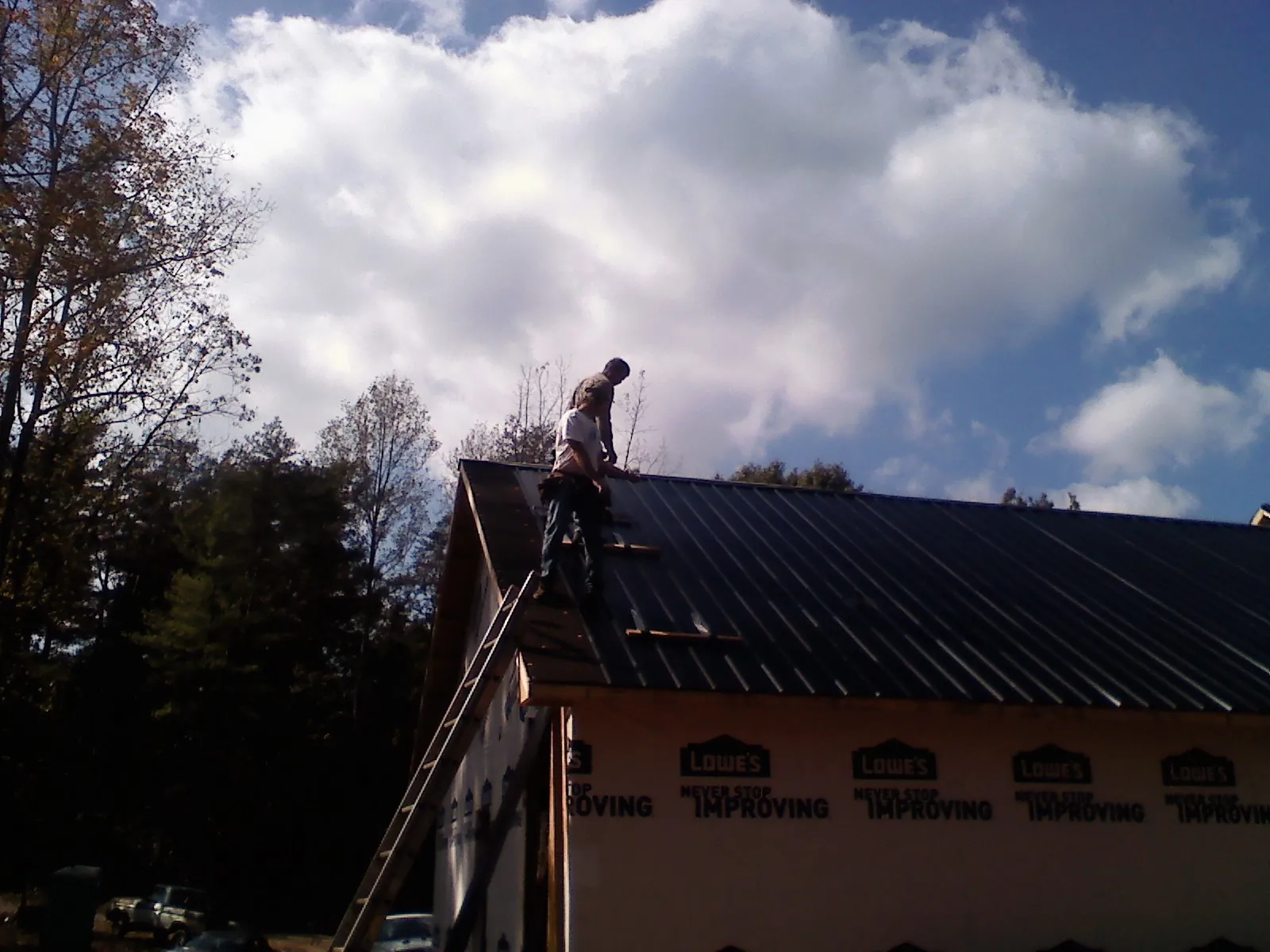 Roofer fastening dark metal panels high against a cloudy sky, from a Roof Inspection job in Culver