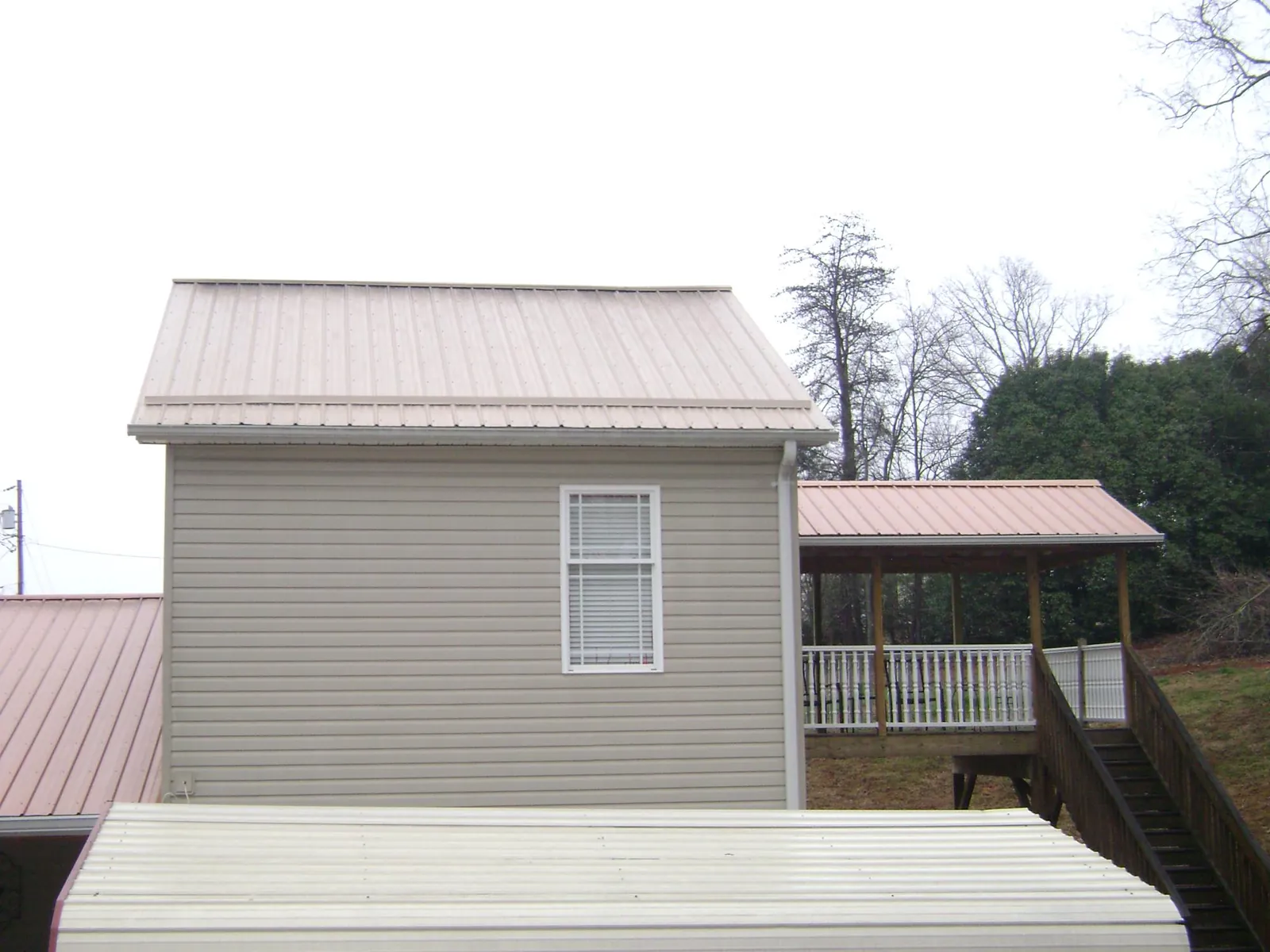 Tan metal roofs on a two story addition and attached porch, from a Roof Replacement job in Culver